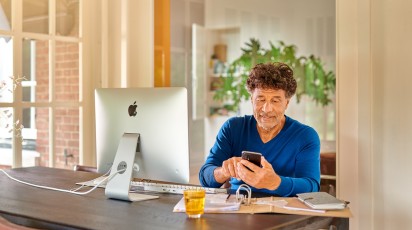 Man zit aan bureau achter computer met telefoon in de hand