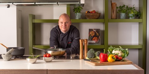 Kok leunt op keukenblad met pannen en ingredienten